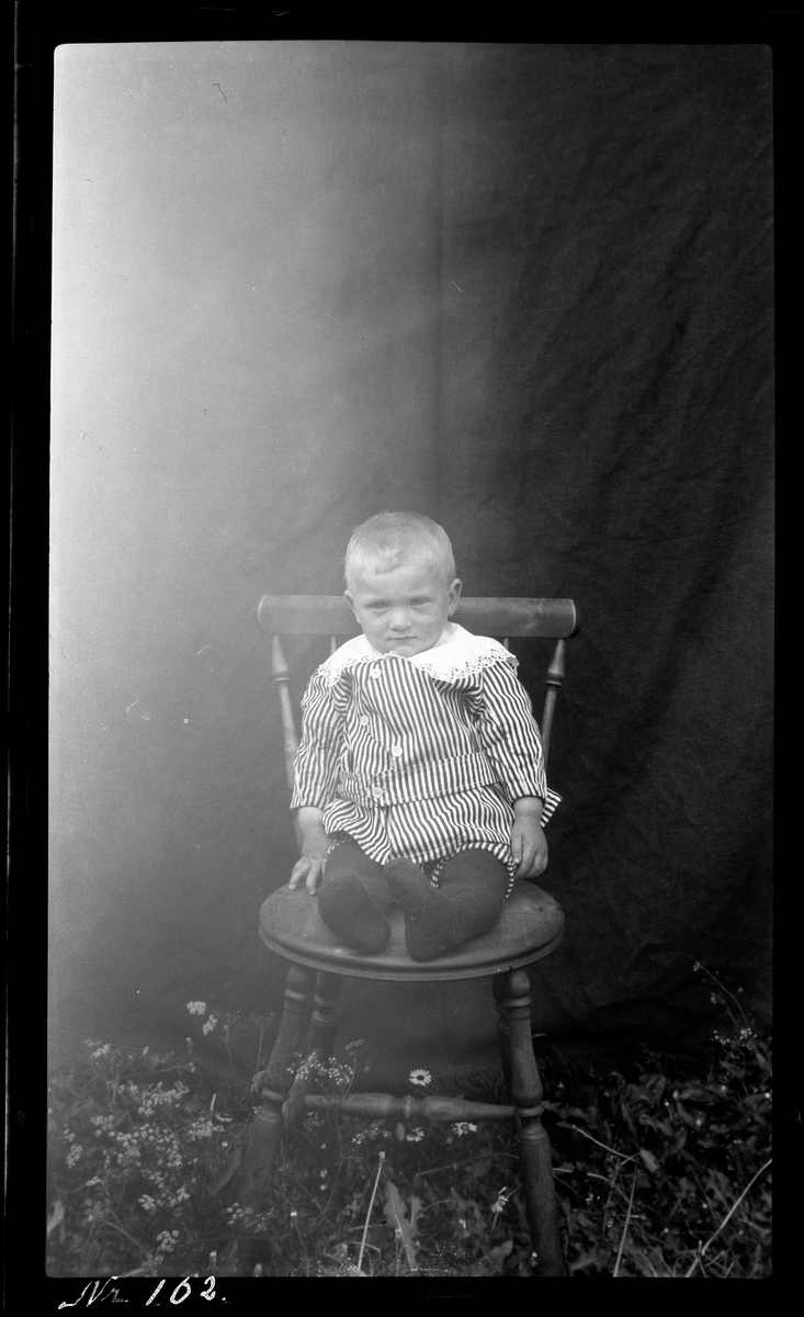 Portrett av en liten gutt sittende på stol.
