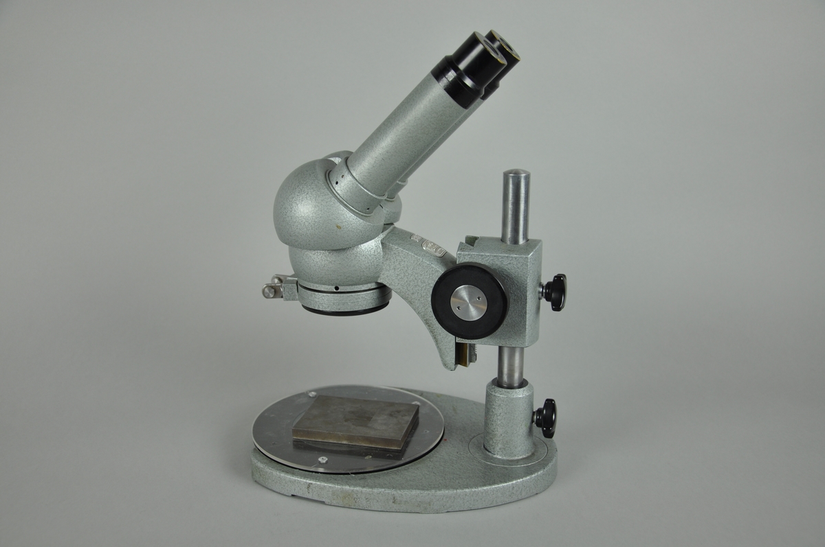 Mikroskop laget i metall. På mikroskpoet er det festet en flatmolett, originalgravyre med gravert motiv.