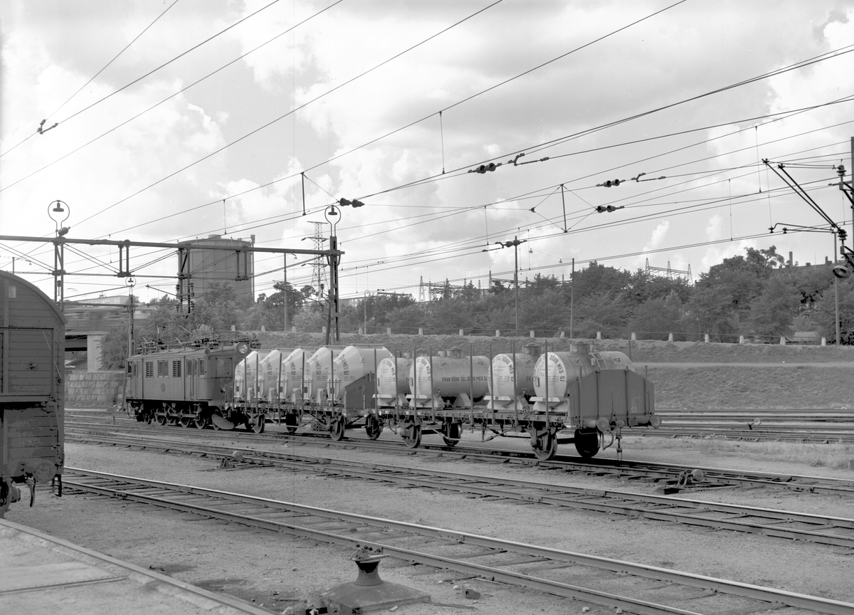 Statens Järnvägar, SJ D lok. Slutna storbehållare av olika typer transporteras på två öppna godsvagnar vid Värtans station. Gasklockan i bakgrunden