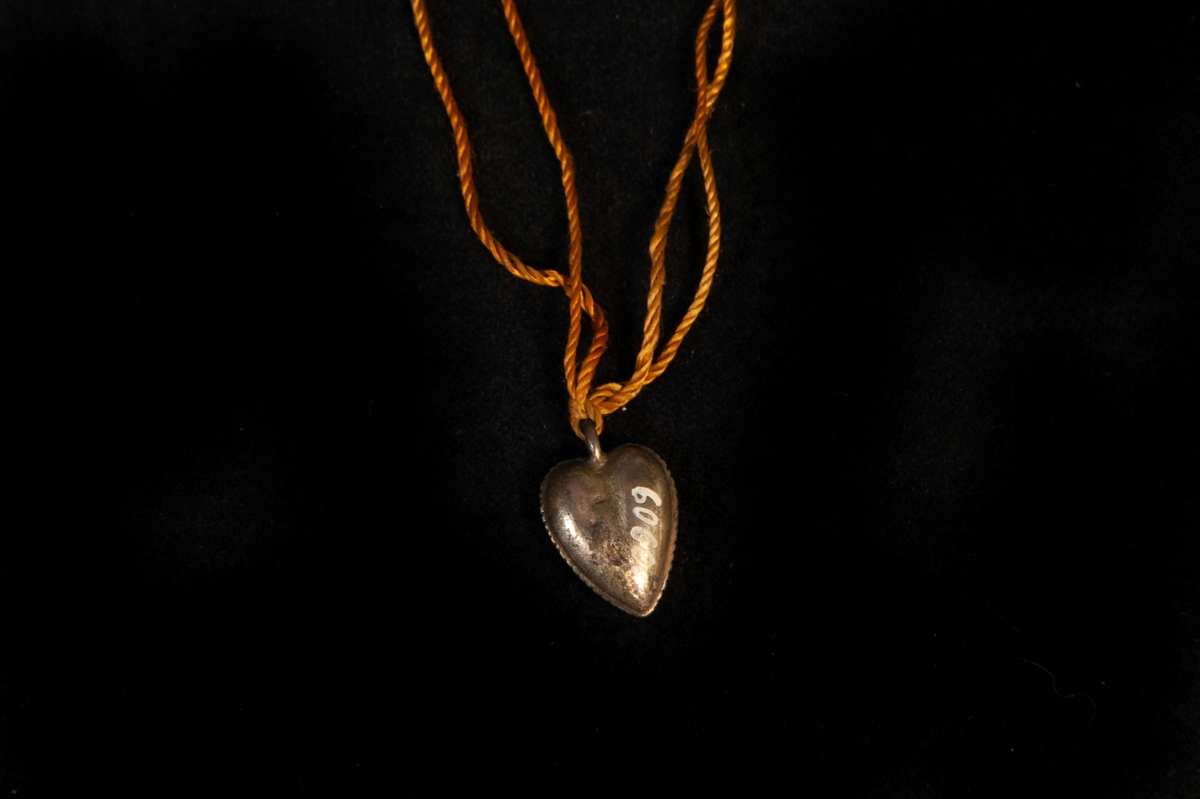 Ett förgyllt hjärta av silver med präglad pärlrand. Hänger i gulorange snodd.