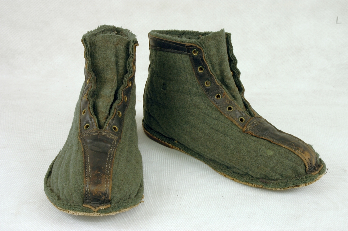 Et par grønne filtsko, sydd av gammel uniformsfrakk, med gummisåler av gamle bildekk. Fra tåa til vrista er skoene forsterka med brunt lær. Seks maljer/hull for snøring. Langsgående stikninger.