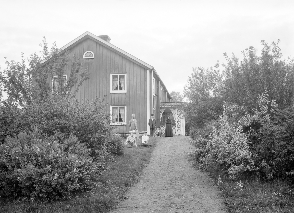 Familjen Palm har ställt upp sig för fotografering invid hemmet Dal i Ingatorps socken. Notera farstukvistens fantasifulla lövsågeri. Tiden är några få år in på förra seklet.