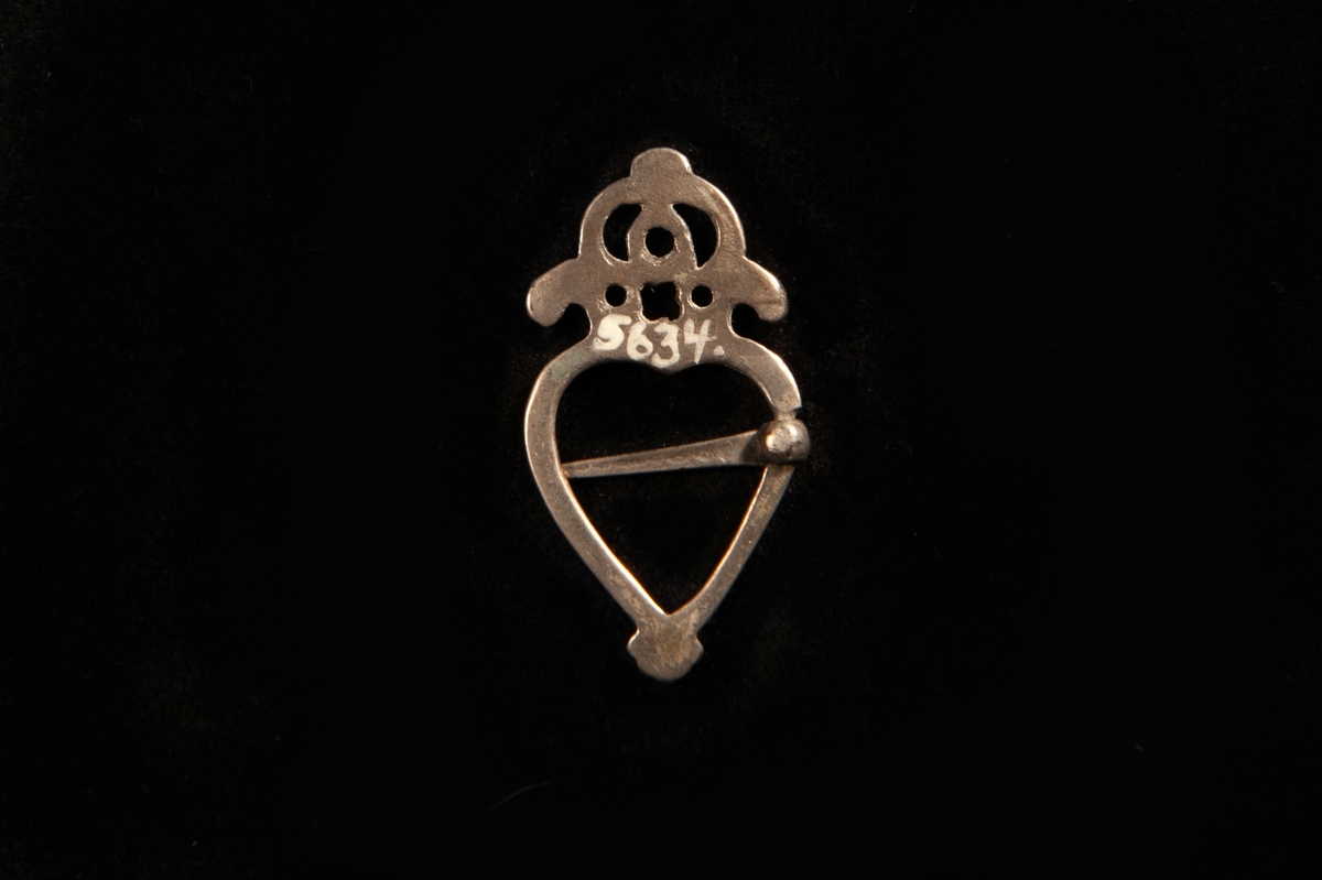 En st. hjärtformad ringsölja av vitmetall med en genombruten krona upptill. Ostämplad.