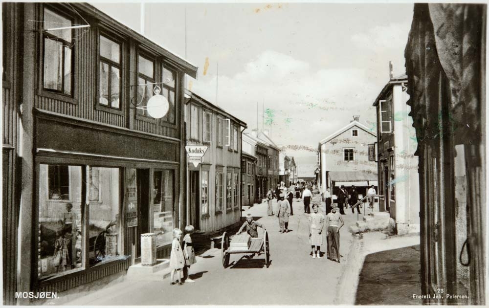 Postkort med motiv fra Sjøgata. Kodak fotobutikk. En del folk i gata. Fiskehall.