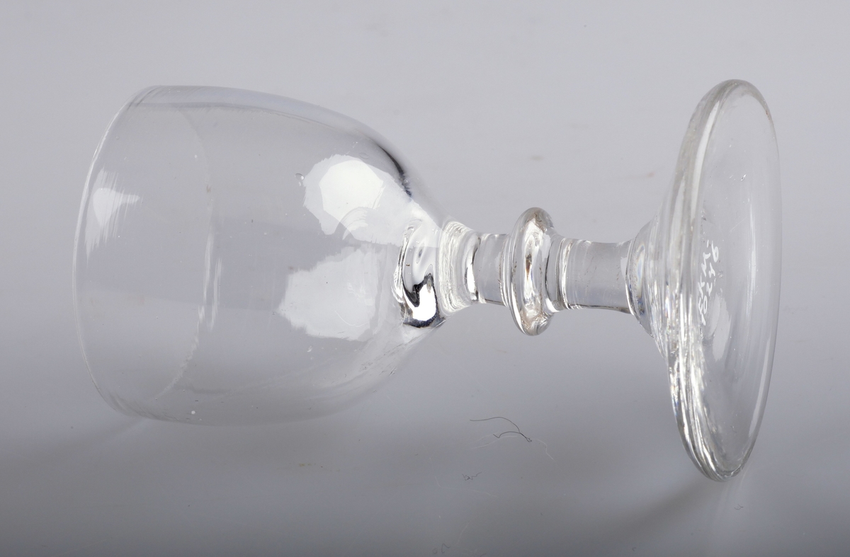 Stettglass blåst i tre deler, med klokke, stett med skive og konkav fotplate. Brutt pontemerke/puntelmerke under. Antatt produsert på Gjøvik Glassverk (1807-1843)
