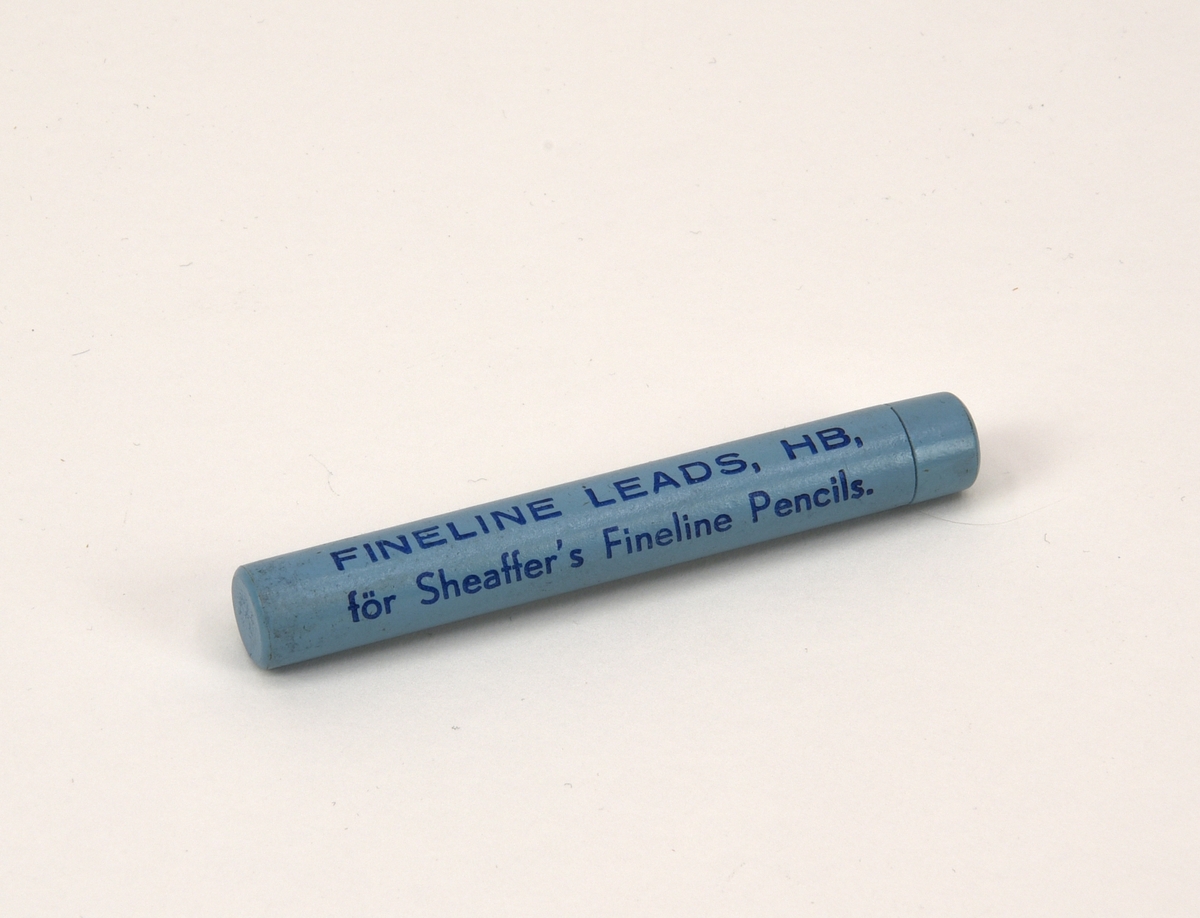 Förpackningsrör av svarvat trä med blyertsstift i HB-hårdhet. Cylindern är målad i en ljusblå nyans och har text i mörkblått: "FINELINE LEADS, HB, för Sheaffer's Fineline Pencils."