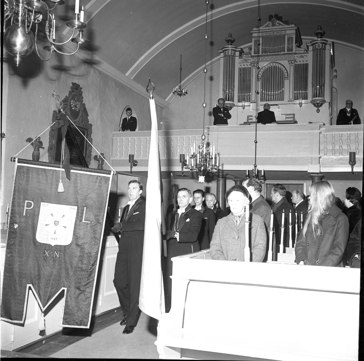 Sällskapet Par Bricole har sammankomst. Män i högtidsdräkt tågar in i Järstorps kyrka med ett standar "P L" i täten.