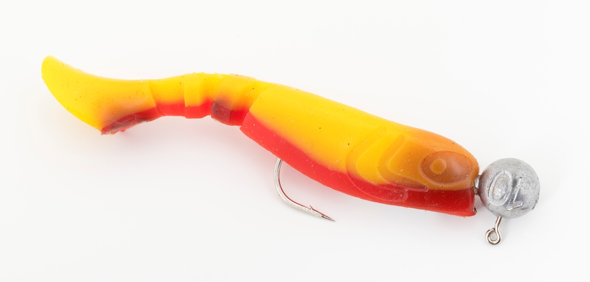 Jigg av gummi, muligens silikon, som er festet på en jiggkrok (jigghode). Kroken, enkeltkroken, som jiggen er festet til er langskaftet og utstyrt med et blyhode støpt fast til krokskaftet, som gir kastetyngde. Kroken stikker opp av ryggen på fiskekroppen.  Jiggen er en fiskimitasjon med flat, gul hale, rød rygg, gul side og underside med innslag av brunt. Denne jiggen kan defineres som en shadjig. I boka Sportsfiskeleksikon (2005) defineres shad som tradisjonell silikonjigg, en fiskeimitasjon med flat hale som skaper et svømmende inntrykk. 



Jiggen brukes til kastefiske med stang der spinnagnet imiterer attraktive byttedyr for fisken.
