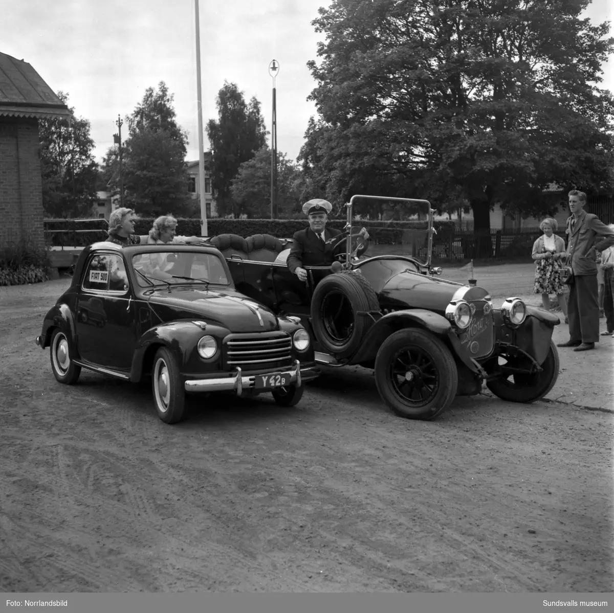 Gamla veteranbilar på planen invid Västra station, Åkersvik. Bland annat Fritiof Larsson med sin Horch invid en liten Fiat 500 med registreringsnummer Y42B, två unga kvinnor tittar upp genom bilens taklucka. På tredje bilden en Ford från 1908, i bakgrunden Kronohäktet.