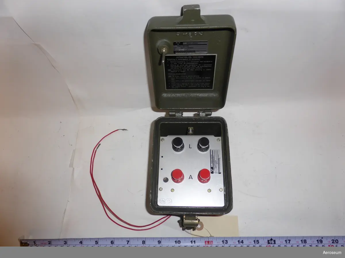 En Tonsvarare i en grön metallåda. I lådan är föremålet silvrigt med två svarta och två röda rattar/knappar. Tillverkad av SATT Elektronik. På lådan finns det en klistrad lapp där det står: "Solrosen" i röd penna. På lådan står det också: "SATT Elektronik STOCKHOLM - SWEDEN". I öppnings- och låsningsmekanismen står det: "NIELSEN HDWE HARTDORD". Inne i locket står det "V549632", "BET M3743-605000 BEN TONSVARARE URSPR- BET SATT 3-5948999 IND- NR 2042", och under detta sitter en lite skylt i locket med instruktion om hur tonsvararen ska användas. På själva mekanismen som sitter fast i lådan står det: "L",  "A", "SATT Elektronik 024", "SATT Elektronik 025", och "BET F6064-000747 BEN TONSVARARINSATS URSPR- BET SATT 52511".