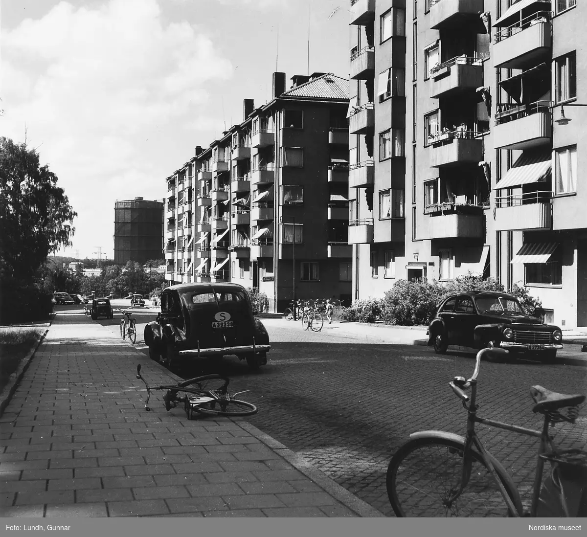 Vy över gata på Gärdet, Stockholm år 1950. Bilar och cyklar är parkerade längs gatan.