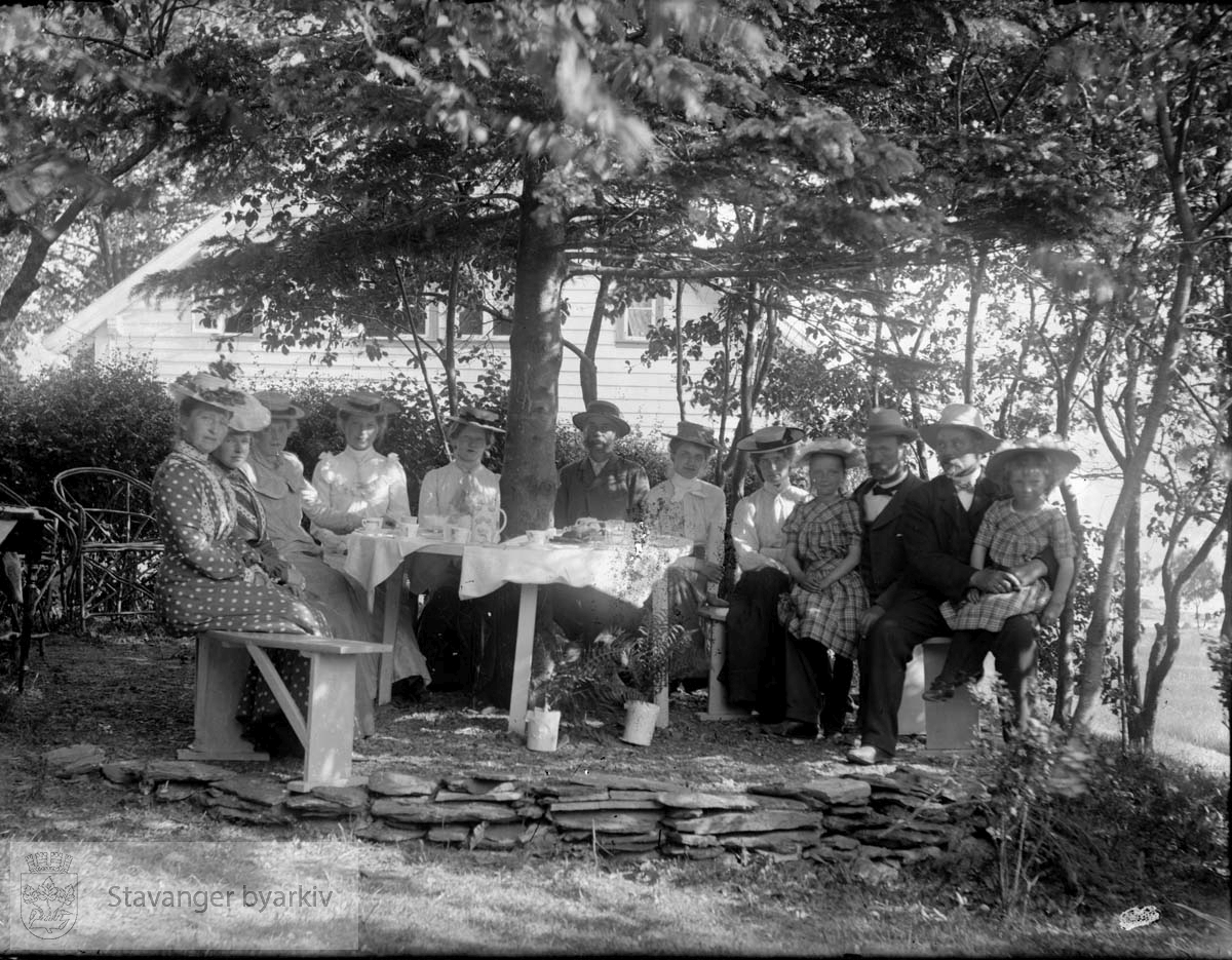 Konsul Chr. Bjelland med familie på besøk hos skipsfører Weidemann Olsen på hans landsted "Sjøheim" på Stord. Her nytes ettermiddagskaffen i hagen en sommerdag i 1902. (Se Minneboken om Stavanger, s. 266)