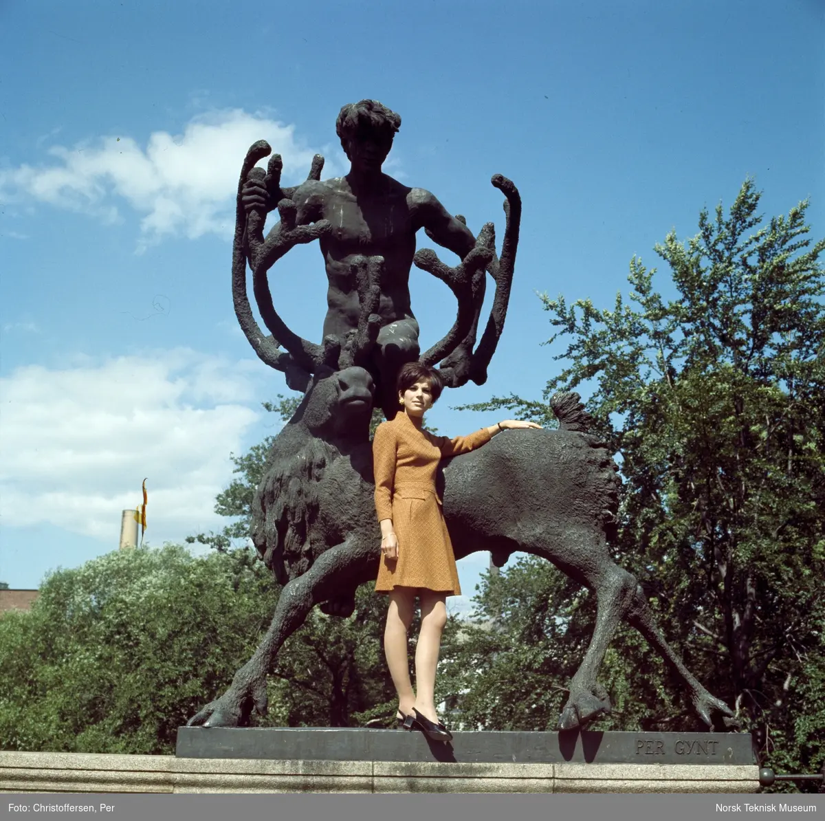 Motebilde i farger. Kvinnelig modell i brun ullkjole av norsk fabrikat, fotografert foran skulpturen "Peer Gynt på reinsdyret" (1933-36) av Dyre Vaa på Ankerbrua/ Eventyrbrua i Oslo, 1968. Bildet er en del av en serie der ett av dem er publisert i ukebladet Det Nye nr. 39, 1968.
