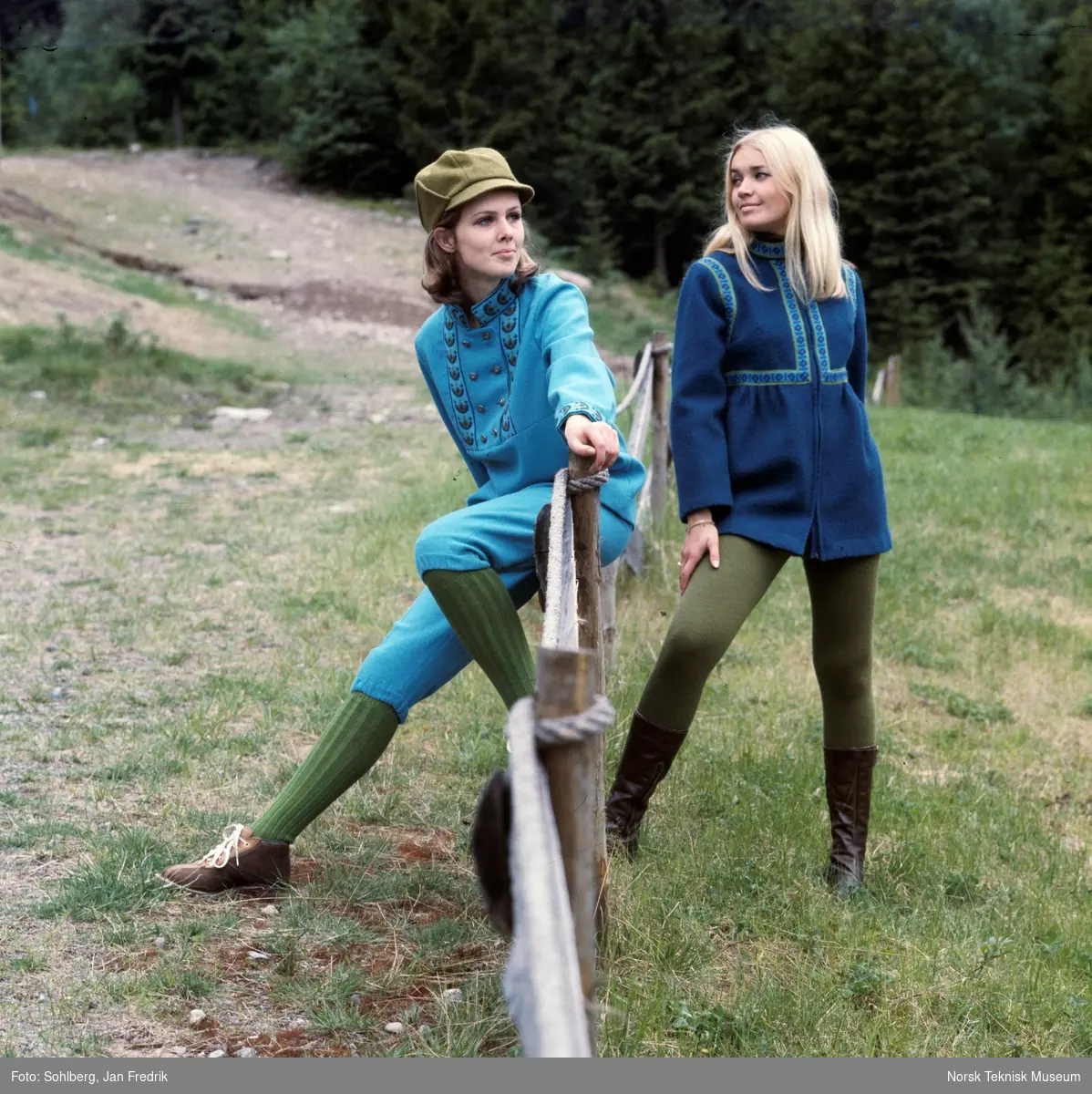 Motebilde, to kvinner ved gjerdet i havnehagen viser klær fra kolleksjonen "Fjord Look", høsten 1968. Bildet er en del av en serie der noen er publisert i ukebladet Det Nye. Billedtekst: "Den lange vamsen med med empirelinje i bakgrunnen har gjennomgående glidelås i fronten og rynker under bysten. De påsydde båndene gir fin vest-effekt. Prisen - i ren ull - er ca. kr. 167,-. Vams og nikkers også i ren ull er farget i "isbre" nyanse. Jakken har dobbeltspent bærestykke med tinnknapper, og "Fjord-look"-bånd markerer bærestykket, offiserskragen og mansjettene. Prisen for vamsen er ca kr 126,-. Nikkersen koster omtrent kr. 73,-."
