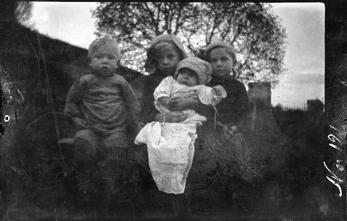 Portrett av fire små barn, fotografert sittende utendørs.