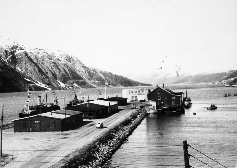 Kan være lokalbåten Vegtind, tilhørende Torghatten Dampskipsselskap, ved Jernbanekaia til venstre bak. Båten foran er trolig DS Saltdal et kombinert laste og passasjerskip bygd i 1884 Stockholm ved navn Transit nr.6, senere Rhea, og omdøpt til Saltdal, da det ble kjøpt av Det Nordlandske Dampskibsselskap i 1945, som var et eget eget selskap med båter i kystfart, skilt ut av Saltens Dampskibsselskap i 1927. Skipet gikk i  rutefart mellom Trondheim, Bodø og Saltdal, reserveskip for hurtigruten mellom 1945-1950. Omdøpt til Meisfjord 1957. Opphugget 1976.