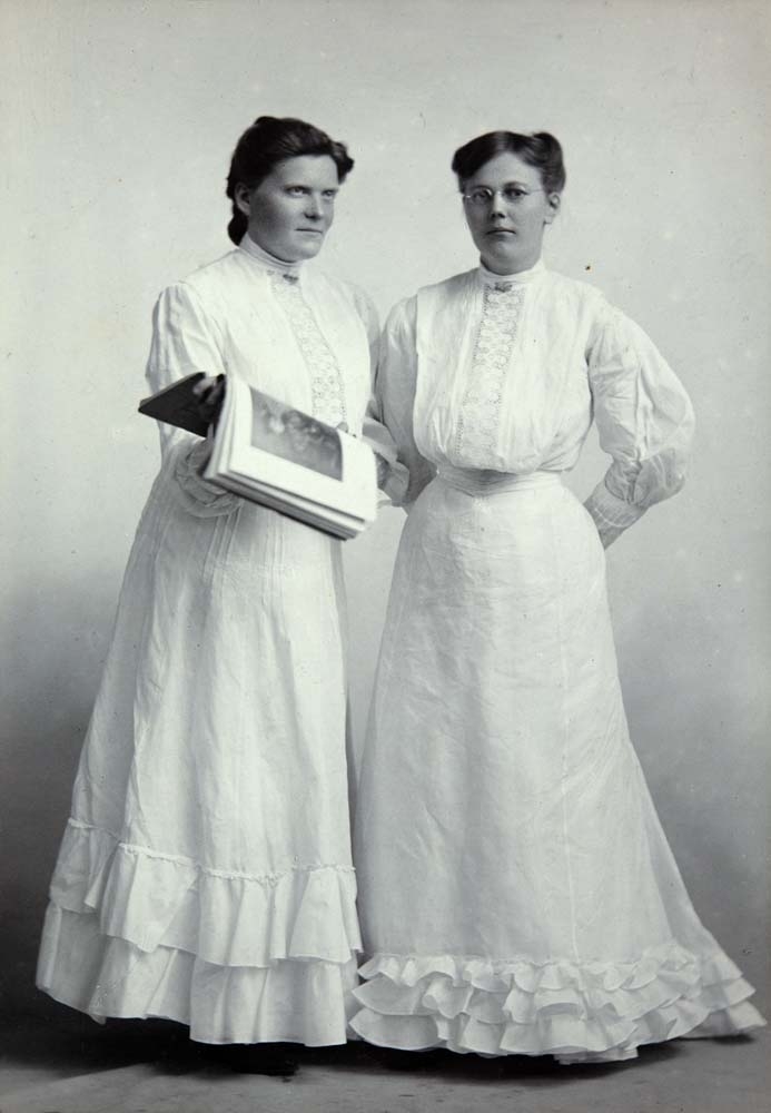 Portrett av to hvitkledde kvinner som holder en stor bok.