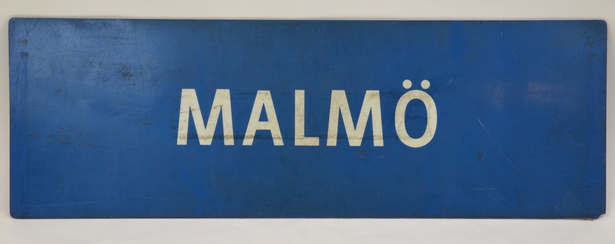 En blå avlång dubbelsidig destinationsskylt som har den vita texten "HÄLSINGBORG C" på ena sidan och "MALMÖ" på den andra.
