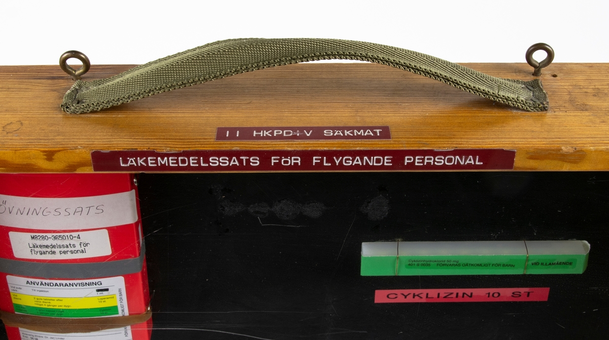 Instruktionstavla med läkemedelssats från för flygande personal. Satsen är monterad i en monter av trä med en framsida av plexiglas. På satsen står det att den expedierades 1994-06.