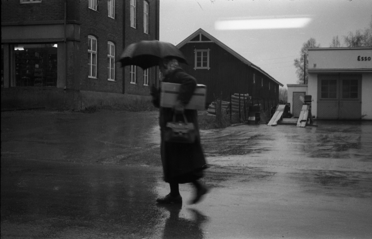 En regntung dag i Lenagata oktober 1957. Personen på bildet er ikke identifisert. Bildet er tatt gjennom vinduet hos Lena Foto & Radio i "Raubua".
