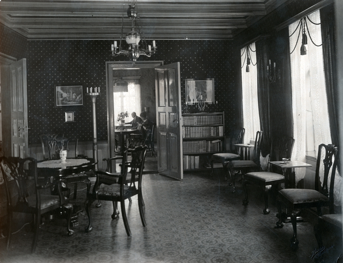 Bildet viser rødstuen med åpne dører inn til røkeværelset til venstre og inn til grønnstuen i midten. Victoria og Christian Anker Bachke sitter ved et bord inne i grønnstuen.