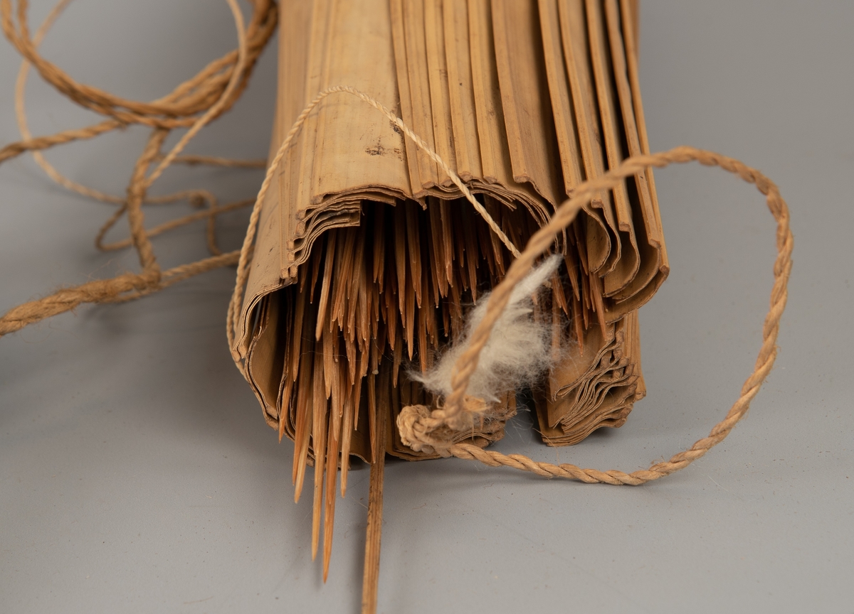 Pilekogger av bambus-spiler, full av piler, et par med bomullsdott i spissen. Tynt flettet tau for feste/oppheng.

Fotografert sammen med tilhørende pose for bomull AAM.19594.D.