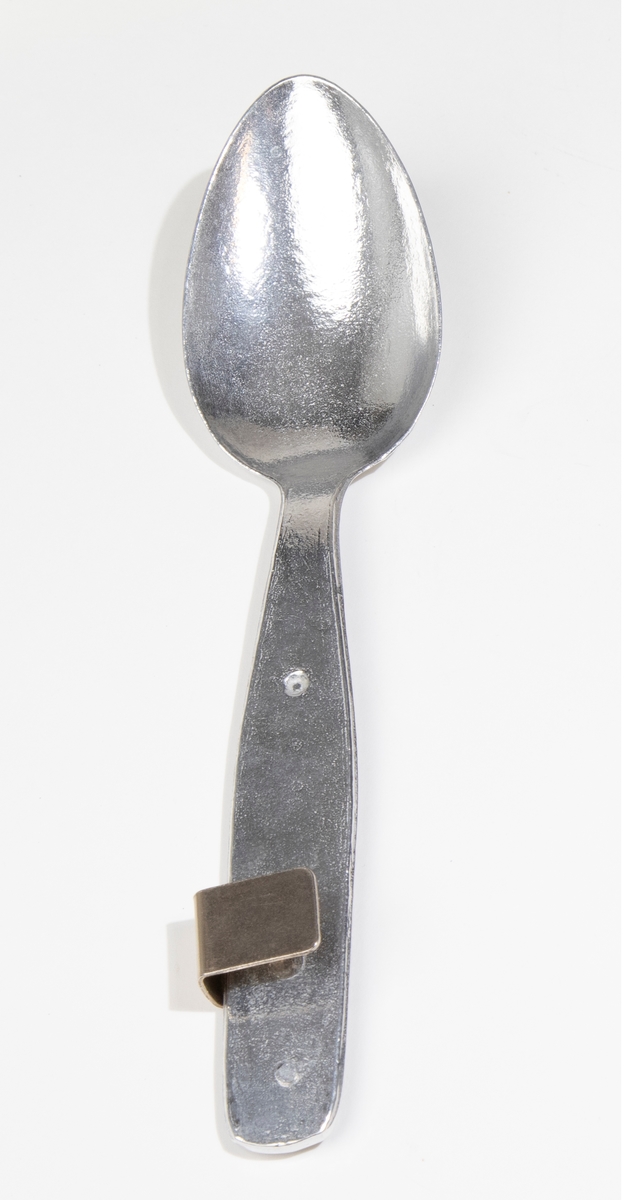 Matsked av lättmetall med fastskruvad liten hållare för att hålla samman skeden med kniven (JM 54960:2) och gaffeln (JM 54960:3). Förpackning: JM 54960:4.