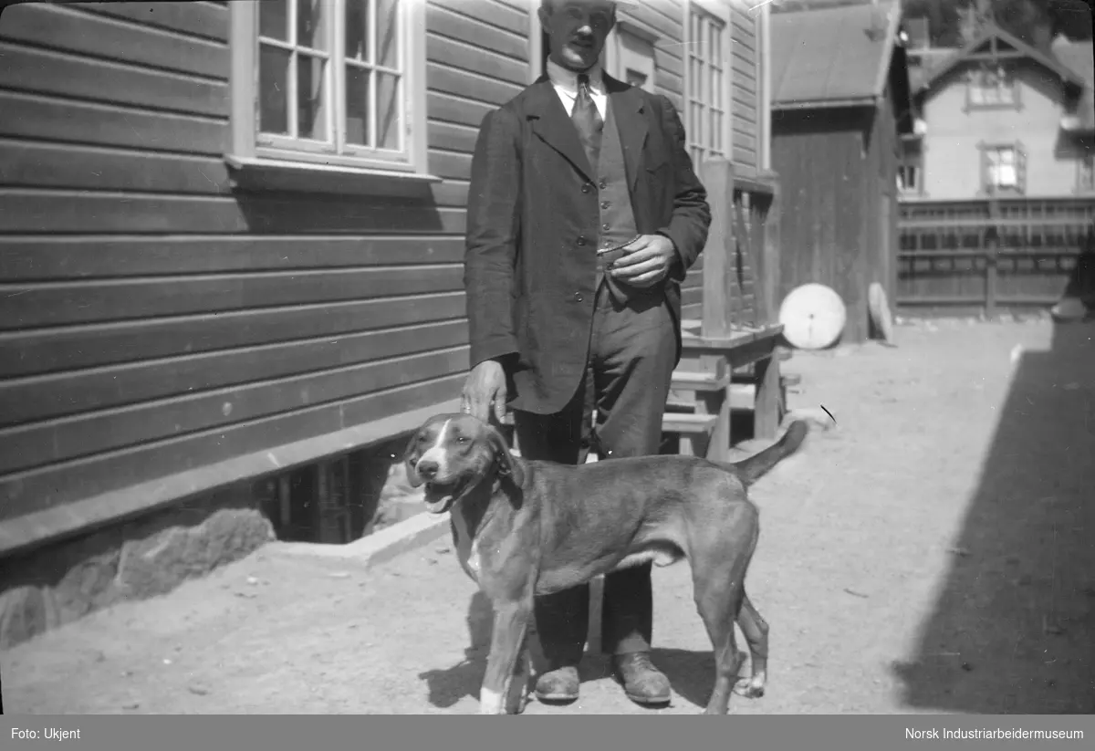Mann i pene klær holder en hund i bakgård