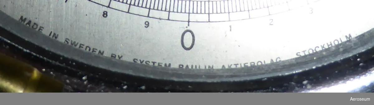 En precisionsmanometer i lackat trähölje, tillverkad av L M Ericsson, med manometer från System Paulin. I lådan sitter en display med en vridbar ratt och nålvisare och en genomskilig slang som sitter fast i ena enden med en metallbit i andra.
