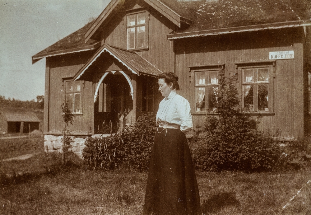 Leirfjord, Breivika. Fint pyntet dame (ukjent) med hvit bluse og mørkt skjørt i hagen foran huset til jordmor Marie Leland.