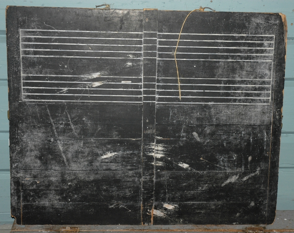 Tavla er limt sammen av flere deler til en stor flate, som er malt sort. Øverst er det skåret inn (relieff) to rader med notelinjer som er malt hvite.