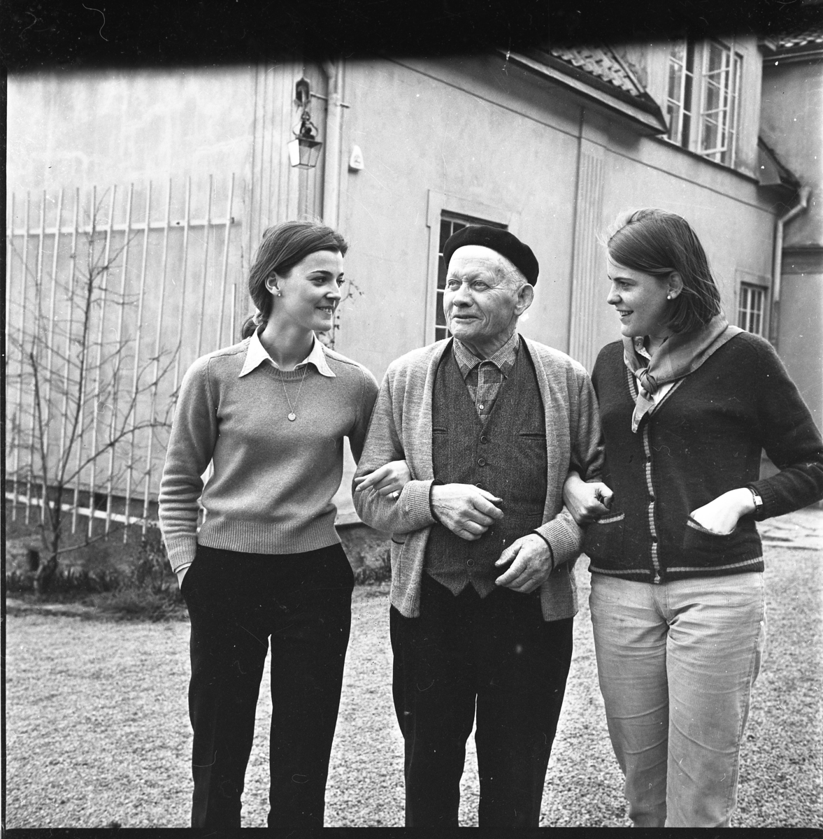 Trädgårdsmästare Ernst Stark med basker på huvudet står i trädgården till Borgmästargården med två unga kvinnor, troligen elever på Grännaskolan.