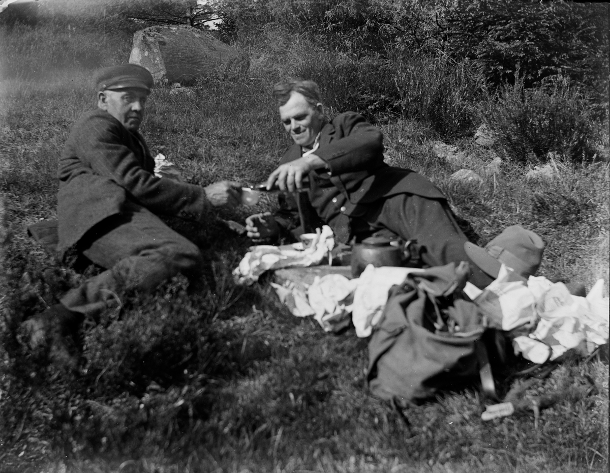 Ett par herrar ligger i en gräsbacke och dricker kaffegök, med kaffepannan mellan sig. Den ene heter Johannes Lundgren.