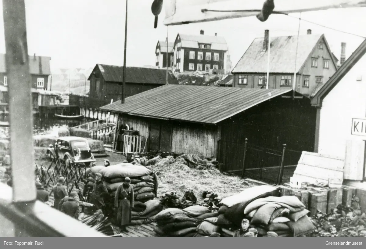 Utsnitt av havna i Kirkenes. Til høyre med deler av skiltet synlig ligger Dampskipsekspedisjonen. Den gamle barneskolen ligger sentralt bak i bildet.