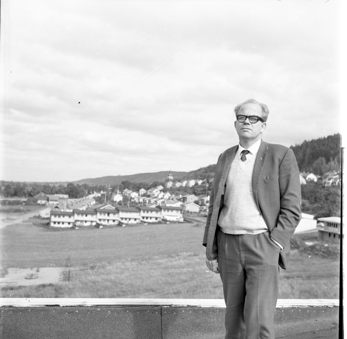 Karl-Erik Johansson med glasögon. Han bär smårutiga byxor, kavaj med ljus v-ringad tröja och slips. Han har vänster hand i byxfickan. Han står troligen på taket till Byggnadsfirman David Johansson i Gränna.