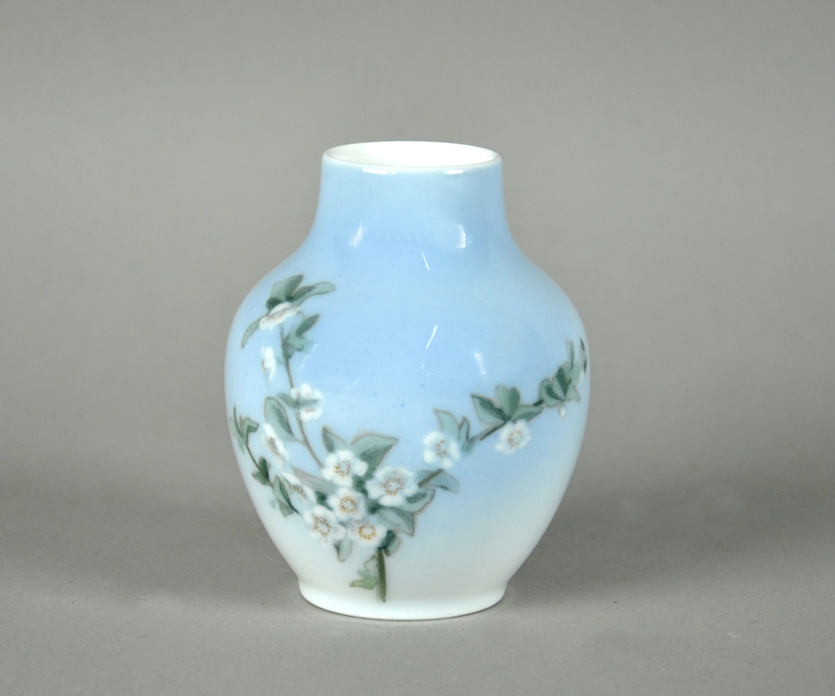 Vase av glassert keramikk, med malt dekor av hvite blomster. Vasen har en utadgående rund form og hals.