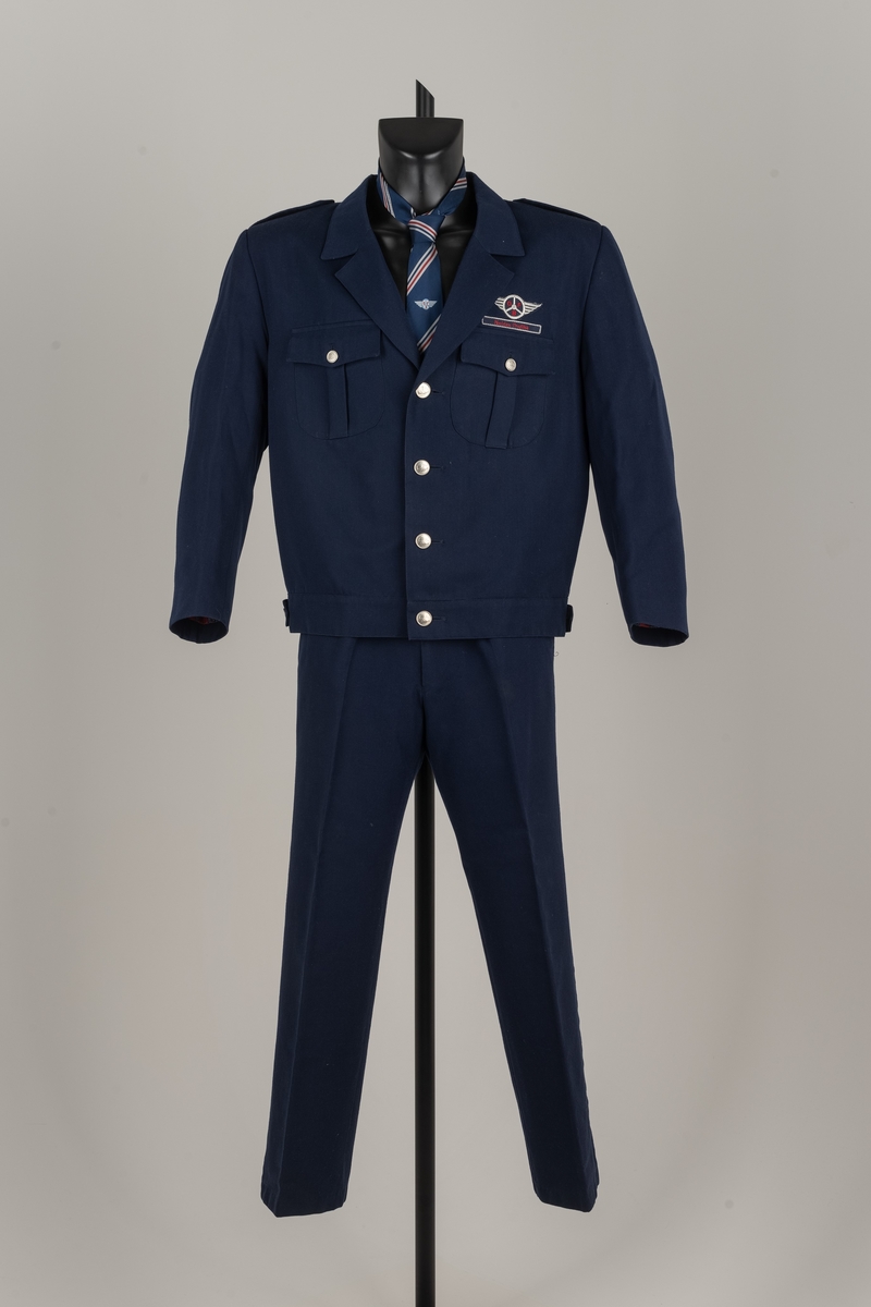 Uniformen består av bukse og jakke i mørk blå ull og polyester. Slips i kunstsilke, mørkeblått med hvite og røde diagonale striper. Pengeveske i ubehandlet lær.