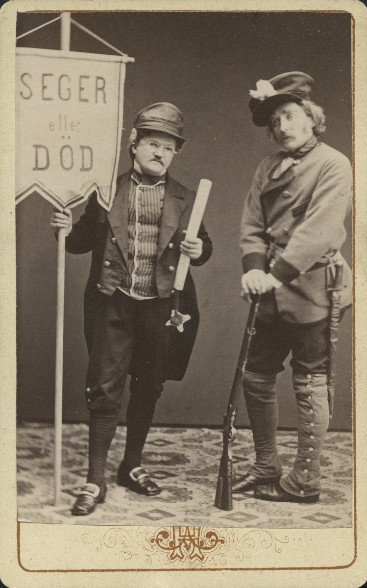 Conny Hedman, Nordström.
Två män iförda teaterklädsel. En håller i ett standar med fana som lyder "Seger eller död".