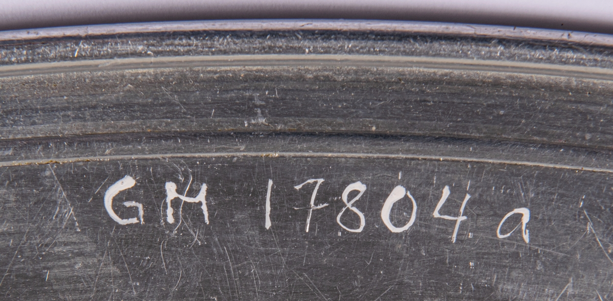 Uppläggningsfat av aluminium. Ovala med slät dekorskåra i brättet.
a: Stämplar (krona) Skultuna 1607 34cm. Mått: 34 x 34cm.