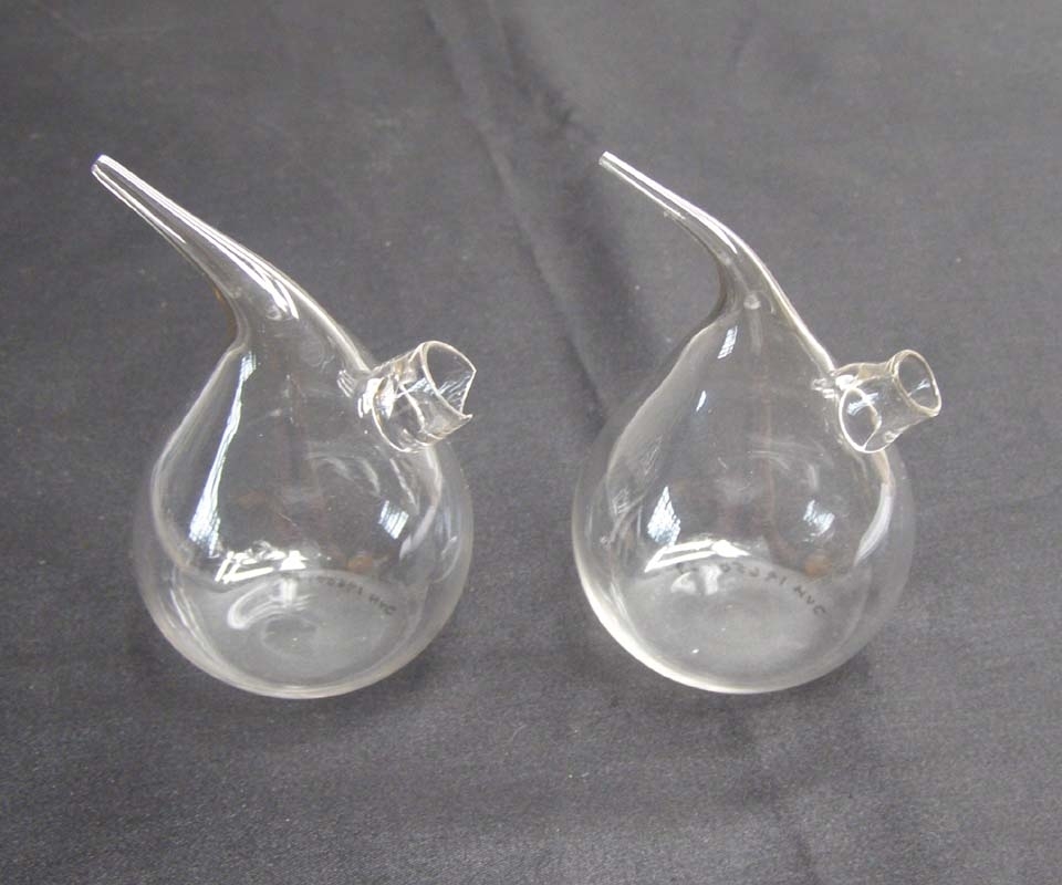 Två glaskolvar av klart glas med droppfunktion och ett litet rör för eventuell påfyllning.
Den ena är skadad i påfyllningsröret.