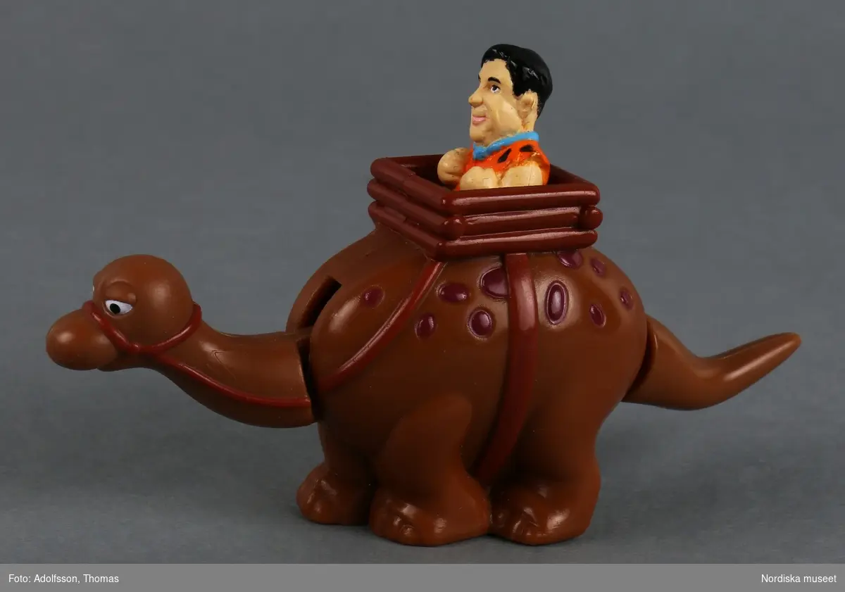 Mekanisk leksak i form av en brun dinosaurie med ryttare som föreställer seriefiguren Fred Flinta. Dinosauriens namn är Dino. Huvudet och svansen är rörliga och om man drar i svansen hoppar gubben upp och ned.