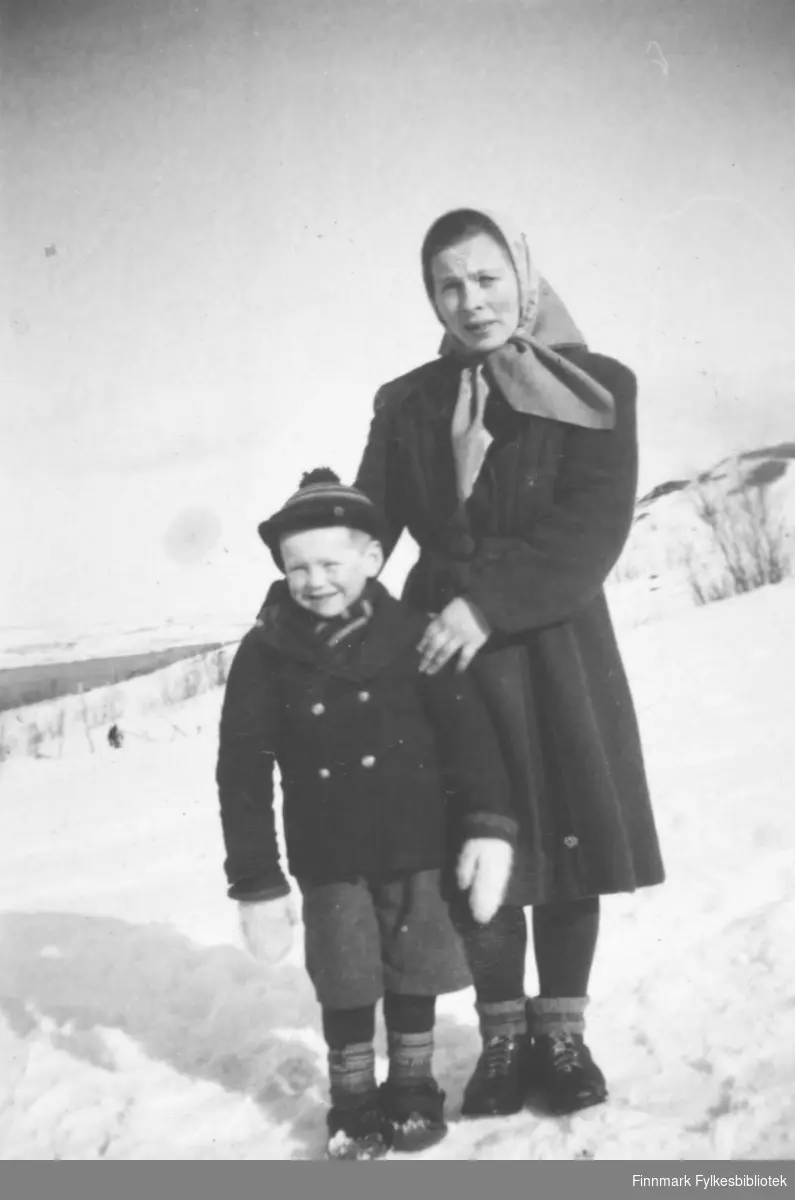 En kvinne og et barn fotografert ute, stående i en snødekt skråning. De er Reidar Mathisen og Bigga Mathisen.