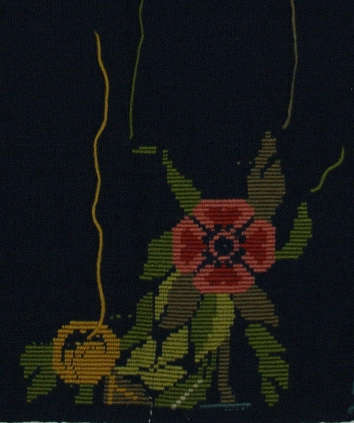 Mörkblå yllelärft, avsedd till stolsdyna. Dynans form markerad med tråckelstygn, ljusblått ullgarn.

Broderiet påbörjat, blad och blommor, s.k. gobelingsöm. Ullgarn i rött, grönt och gult.

Lärftet har en stadkant, sydd med kaststygn på övriga tre sidor.