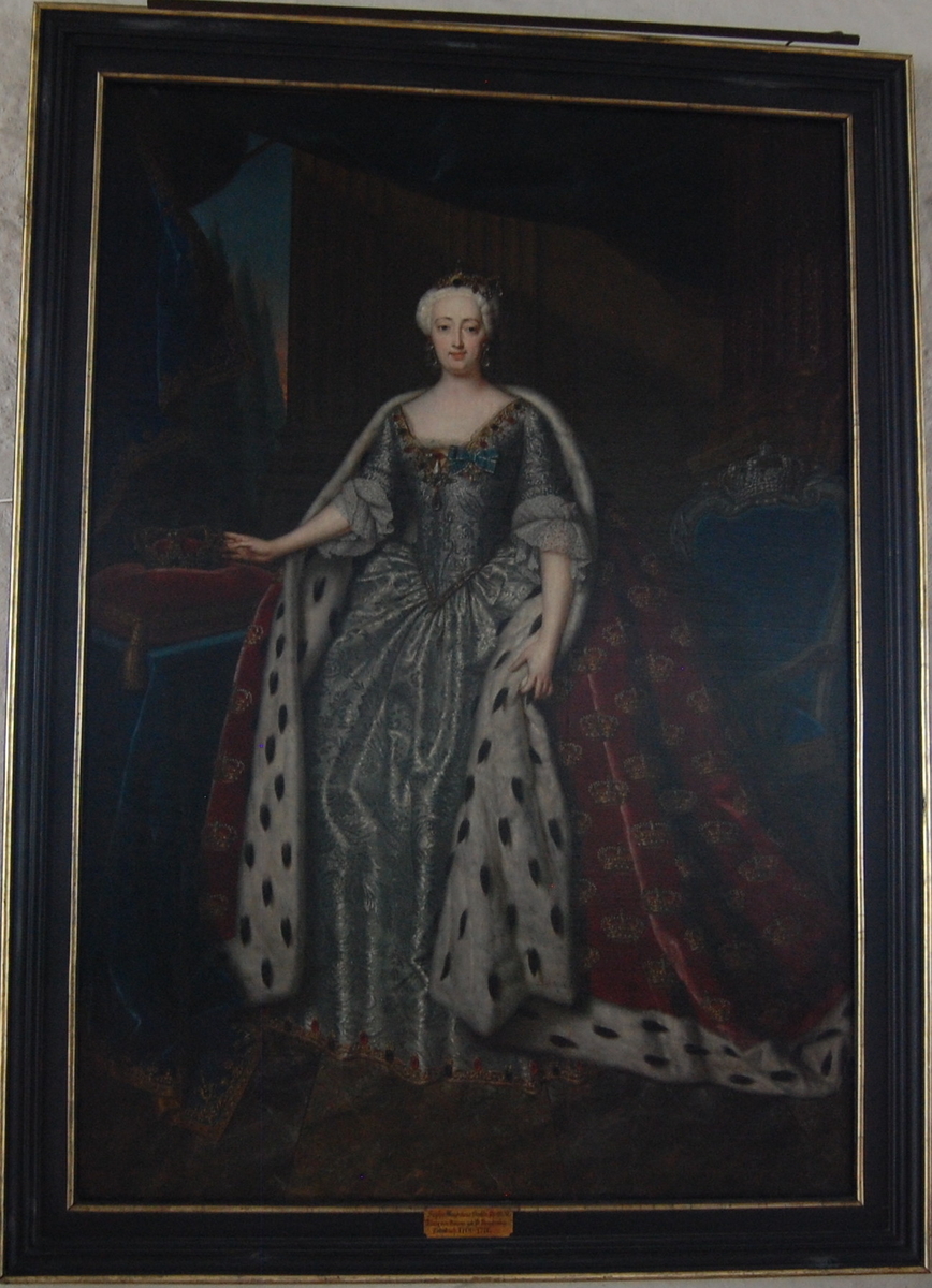 Portett av dronning Sophie Magdalene, gift med kong Christian VI av Danmark, i helfigur stående i interiør. Ikledd en sølvkjole og en rød kappe med hermelinpels, dekorert med kroner.
