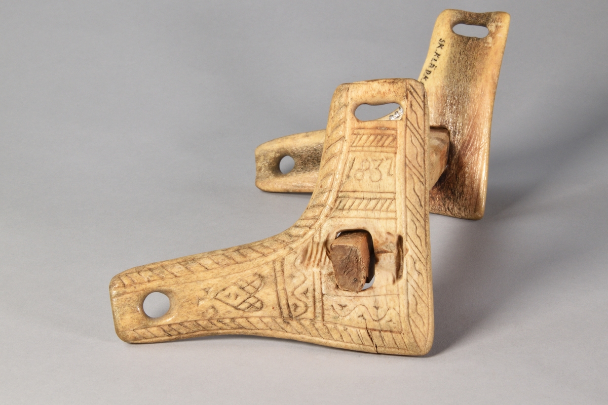 Munbett av trä, rakt, med två vinklade rörliga sidostycke av horn. Rik ornamentik på sidostyckena.