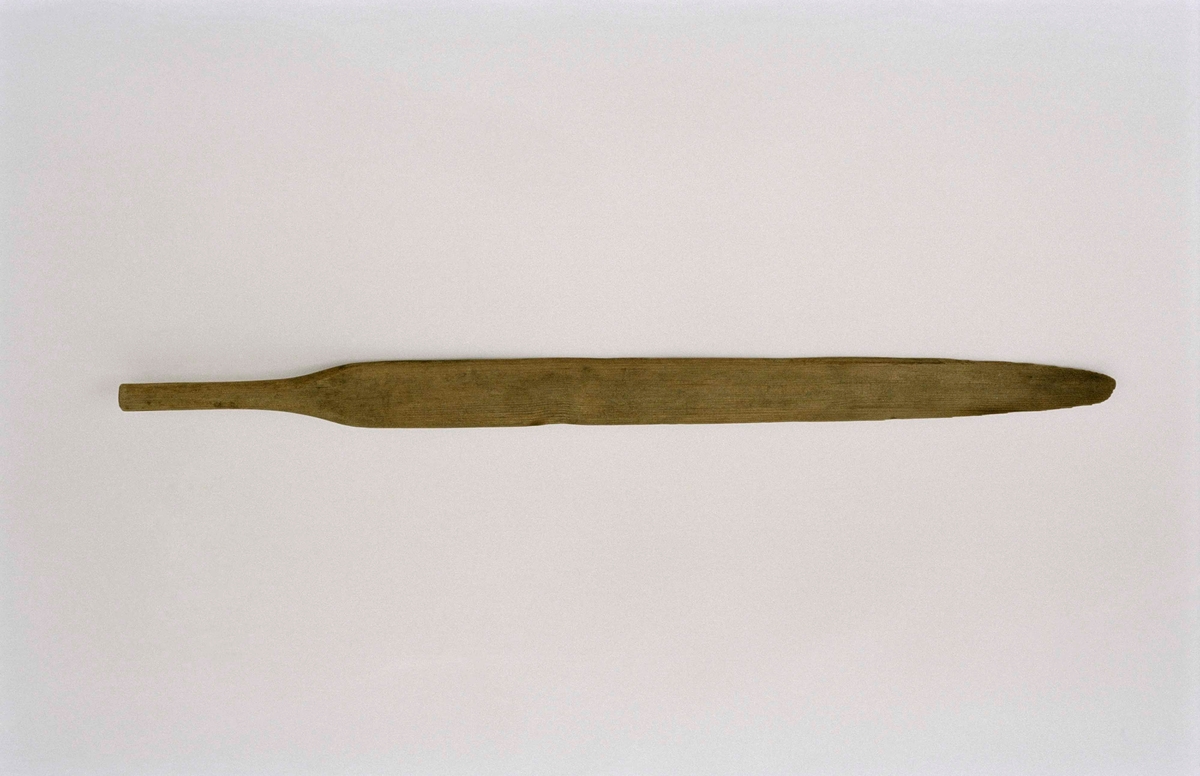 Brödspade av trä i ett stycke. Långt svärdformigt blad, kort runt skaft.