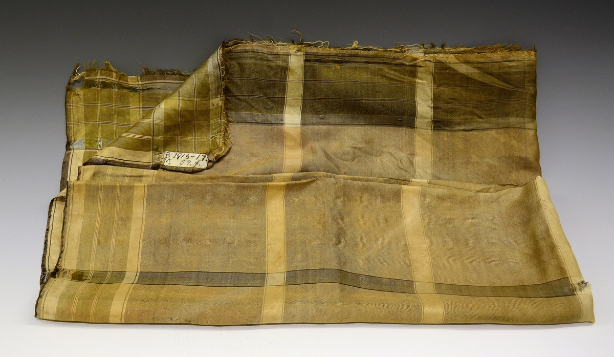 Silketørkle tilhører TGM-BM.1916-17:059 A-K.
Fra protokollen: Kvendeklædning fraa Heitdal, sauma til brurebunad i 1860-aari: F) Rutut silkeplagg til skautet.
Kvadratisk silketørkle.