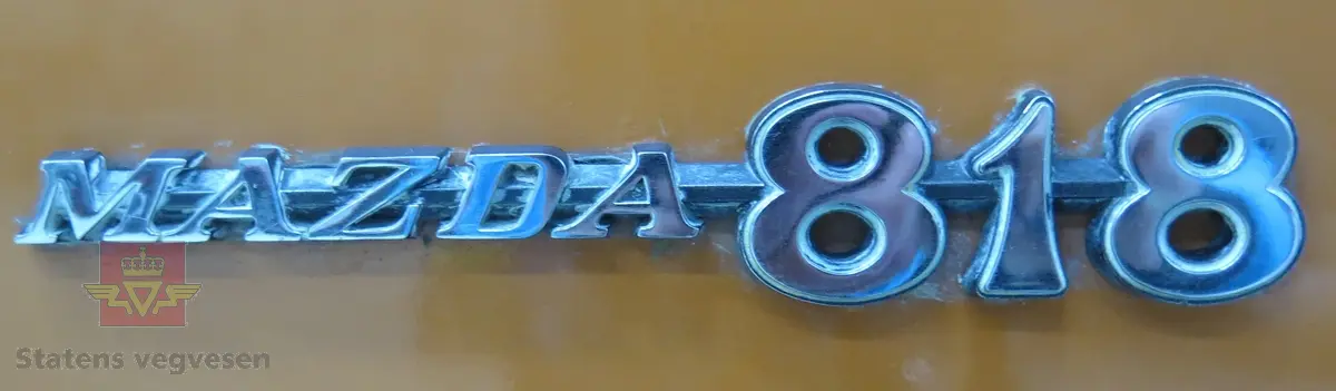 Mazda 818 Deluxe. 4-dørs sedan karosseri, oransje (Herschel Orange) lakk utvendig. Svart interiør med hvitt taktrekk. Bilen har en SOHC, vannavkjølt, bensindrevet 4-sylindret rekkemotor med et sylindervolum på 1272 kubikkcentimeter. Enkel forgasser. Motorytelse/effekt 69 hk. To aksler, bakhjulstrekk. 4- trinns manuell girkasse med girstang i gulvet. Antall sitteplasser er 5. Km. stand på telleren er 7384 km (i virkeligheten rullet 107 384 km). Standard dekkdimensjon foran og bak er 155 SR 13. Felgene er 4.5 " brede.