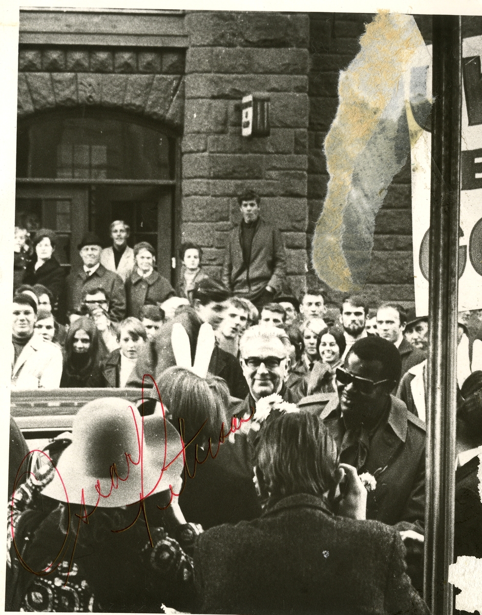 Fra Olaf T. Ranum's "kunstnervegg". Jazzpianisten Oscar Peterson  (til høyre med solbriller) blant skuelystne i en gate (sannsynligvis i Trondheim). Olaf T. Ranum med briller midt i bildet.