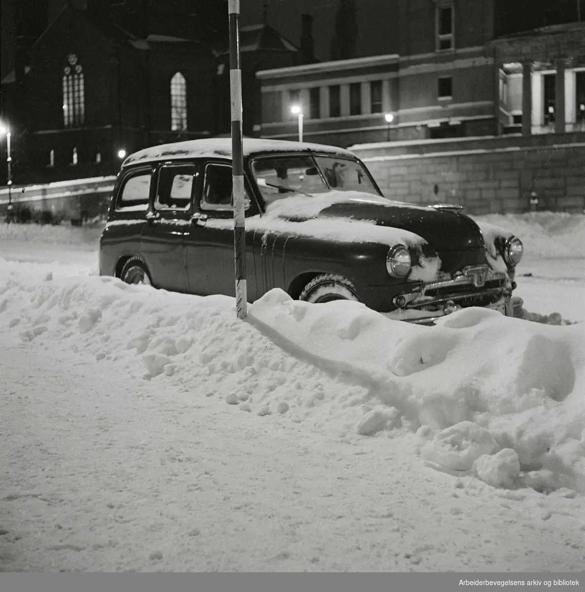 Parkert bil med snø på Arne Garborgs plass. Trefoldighetskirken og Deichmanske bibliotek i bakgrunnen. Desember 1959.
